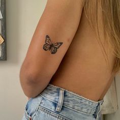 a woman with a butterfly tattoo on her arm and shoulder, standing in front of a mirror