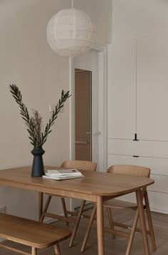 a wooden table with two chairs and a vase on it next to a white cabinet