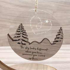 a wooden ornament with an image of trees and the words, the sky looks different when you have someone's love up there