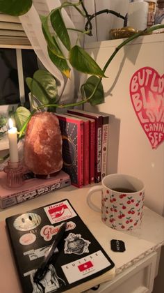 a coffee cup and some books on a table with a plant in the corner next to it