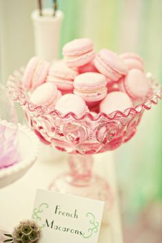 pink macaroons in a glass bowl on a table with a name tag and other items