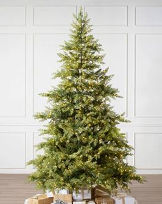 a small christmas tree with presents under it on the floor in front of a white wall