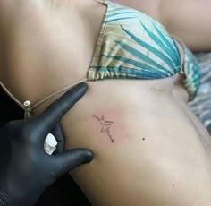 a woman's stomach with a tattoo on her left side, and a black glove in the foreground