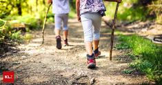 two people walking down a dirt path with poles in their hands and backpacks on