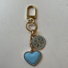 a blue heart shaped keychain hanging from a gold colored metal hook on a white surface