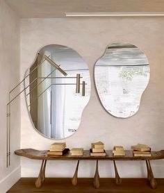 two mirrors on the wall above a table with books