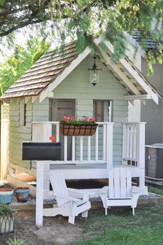 a small white house with a porch and lawn chairs in front of it, next to a tree