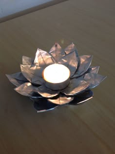 a candle that is sitting on top of a metal flower shaped bowl with spoons in front of it