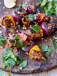 a wooden cutting board topped with meat and veggies on skewered skewers