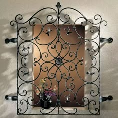 an iron window frame with flowers and candles on the windowsill in front of a mirror