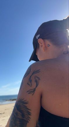 a woman sitting on the beach with her back turned to the camera, wearing a baseball cap