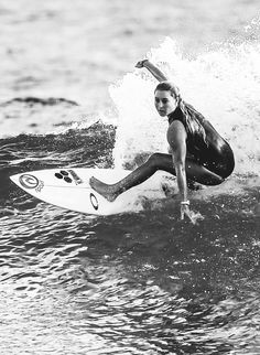 a woman riding a surfboard on top of a wave in the ocean with her arms out