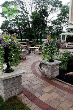 an outdoor patio with brick pavers and flower pots on the ground, surrounded by tables and chairs