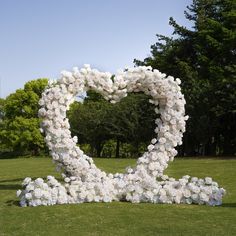 a heart shaped sculpture made out of white flowers in a park with trees in the background