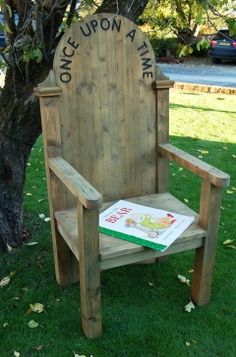 a wooden chair sitting in the grass with a book on it's lap next to a tree