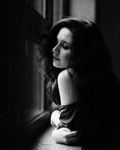 a black and white photo of a woman leaning on a window sill looking out the window