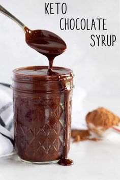 a spoon full of keto chocolate syrup being poured into a jar with cinnamons in the background