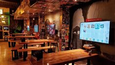 an empty restaurant with wooden tables and benches in front of a flat screen tv on the wall