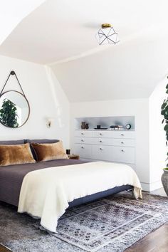 a bedroom with a bed, dresser and mirror on the wall next to a potted plant