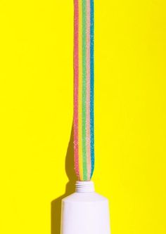 a toothbrush sticking out of a white cup on a yellow background with rainbow stripes