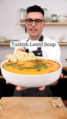 a man holding a bowl of soup with bread on the side and words that read, turkish lentil soup