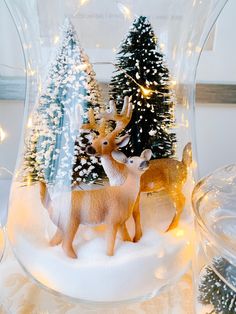 two deer figurines in a snow globe with christmas trees and lights behind them