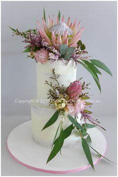 a three tiered cake with flowers and greenery on the top is decorated in white frosting