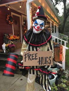 a creepy clown holding a free hugs sign in front of a house decorated for halloween