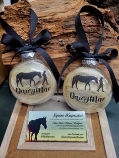 two glass ornament with horse silhouettes on them in front of a log