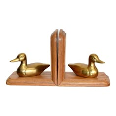 two brass ducks are sitting next to each other on a wooden bookend with a white background