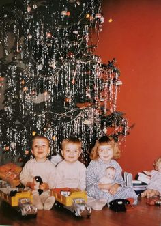 three children sitting in front of a christmas tree