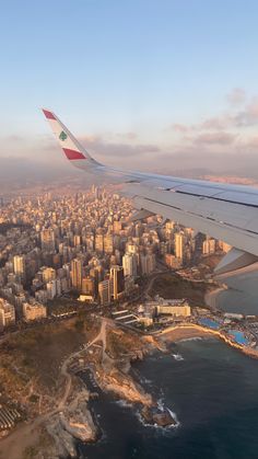 the wing of an airplane flying over a large city next to the ocean and beach