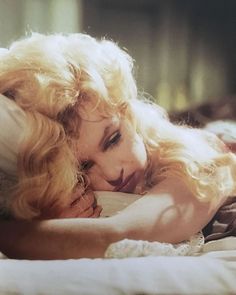 a woman laying on top of a bed next to a man with long blonde hair