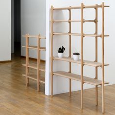 two wooden shelves with plants in them on the floor next to a white wall and wood floors