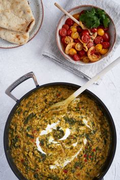 a pan filled with spinach and tomatoes next to a bowl of pita bread