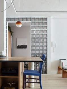 a blue chair sitting next to a wooden table in a living room under a light fixture