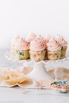 cupcakes with pink frosting and sprinkles on a cake stand