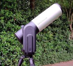 a telescope on a tripod in front of some bushes