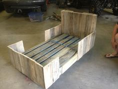 a bed made out of wooden pallets in a garage with a woman sitting next to it