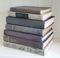 a stack of old books sitting on top of each other in front of a white wall