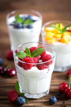 two glasses filled with yogurt and berries on top of a wooden table next to fruit