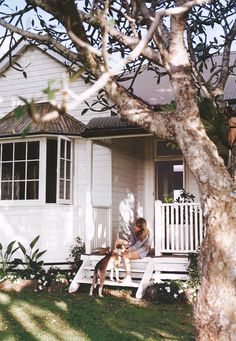 a woman sitting on a porch with her dog in front of the house next to it