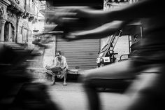 black and white photograph of a man sitting on a bench in front of a building