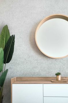 a round mirror hanging on the wall above a white dresser with potted plant in it