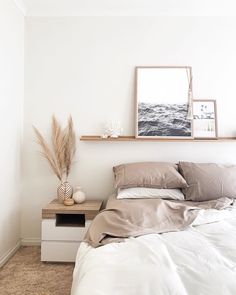 a bed with white sheets and pillows next to a wooden shelf on the wall above it