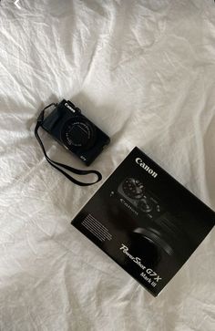 a camera sitting on top of a white sheet next to a box with the instruction manual