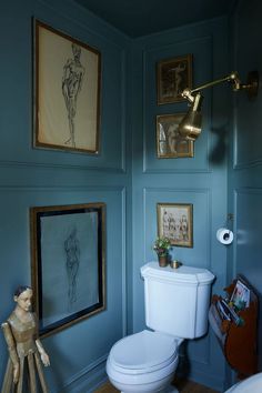 a bathroom with blue walls and pictures on the wall above the toilet, along with a wooden floor