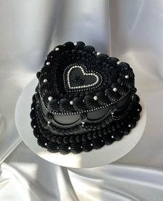 a black and white heart shaped cake on a plate with silver bead trimmings