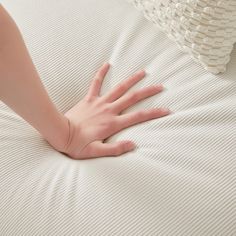 a person's hand on top of a bed with white sheets and pillows in the background