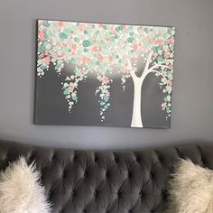 a couch with two pillows and a painting on the wall above it that has a tree painted on it